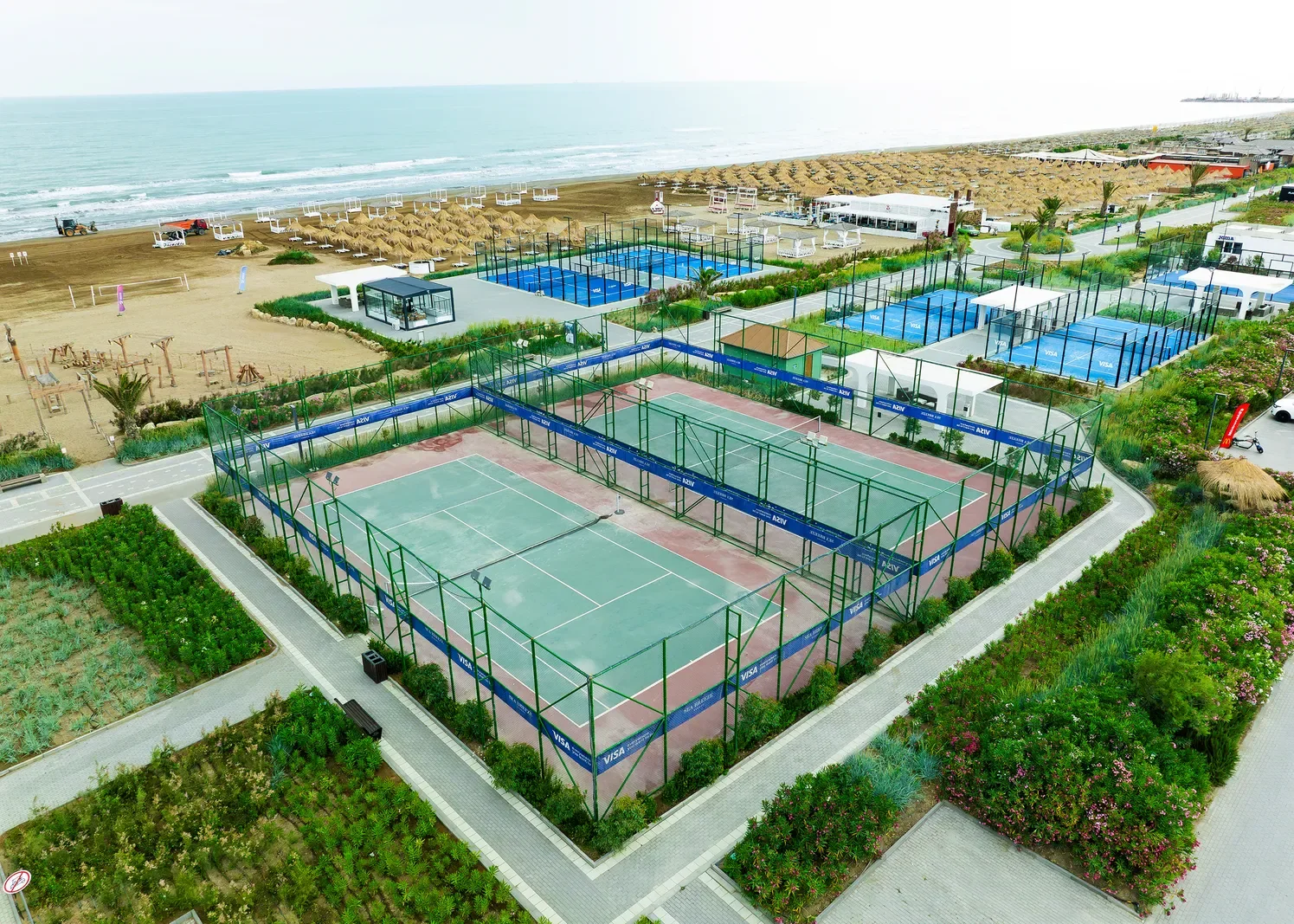 Спортзона Sea Breeze сверху: слева на песке — деревянный зал, в центре теннисный корт, за ним падел-корты и пляж
